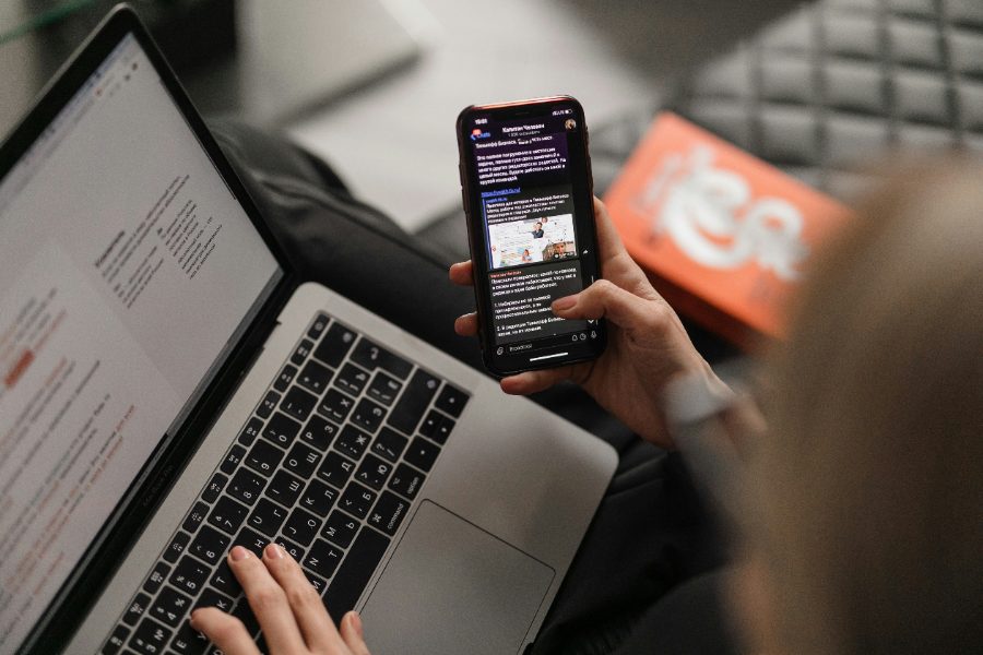 Person using a phone beside a laptop